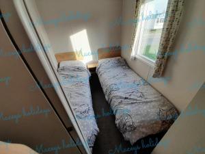 two beds in a small room with a window at Pet friendly caravan in Walton on the Naze in Walton-on-the-Naze
