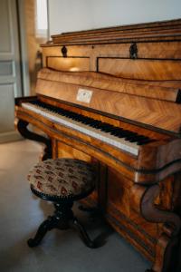 - un piano en bois avec un tabouret à côté dans l'établissement Les Granges Pelloquin, à Bernières-sur-Mer