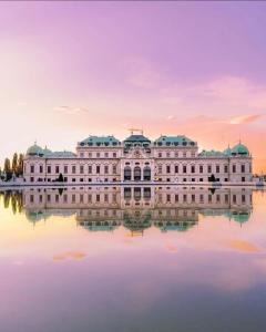 ein großes weißes Gebäude auf dem Wasser bei Sonnenuntergang in der Unterkunft Apartment 5 min Schönbrunn Gloriette, Direct to City Center, Free Parking in Wien