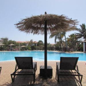 two chairs and an umbrella in front of a pool at Poolside Serenity at Tortuga Beach - 491 in Prainha