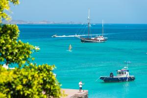 un hombre de pie en un muelle con un barco en el agua en 4rooms Fuerteventura en Corralejo