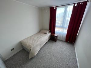 a bedroom with a bed and a window with red curtains at Cozy Apartment Near Airport, Secure, and Versatile in La Serena