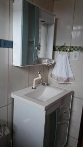 La salle de bains est pourvue d'un lavabo, d'un miroir et d'une robe. dans l'établissement Casa B com Piscina Enseada Ubatuba Max06 Hosp, à São Francisco do Sul