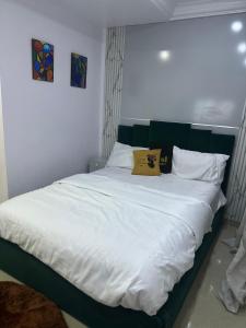 a large bed with white sheets and a yellow pillow at Daisies in Lekki