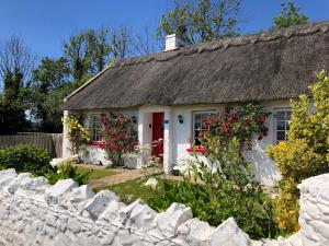a white cottage with a thatched roof and a stone fence at Clannad Cottage in Arboe