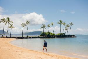 ホノルルにあるThe Kahala Hotel and Resortの椰子の木が生える浜辺を歩く男