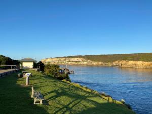 eine Bank, die auf dem Gras neben einem Wasserkörper sitzt in der Unterkunft Southern Ocean Motor Inn in Port Campbell