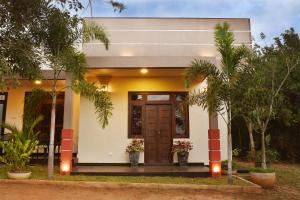 uma casa branca com uma porta castanha e árvores em Leaf Dew Resort em Anuradhapura
