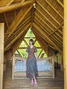Una donna è in piedi su un ponte di legno di Sun Sang Eco Retreats a Tabanan