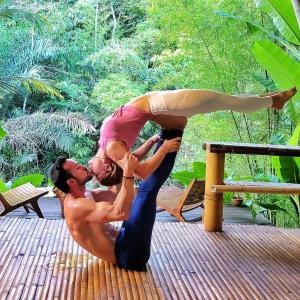 Un uomo e una donna che fanno yoga su un ponte di Sun Sang Eco Retreats a Tabanan