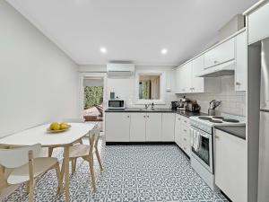 アデレードにある'The Lemon Tree' North Adelaide Character Cottageの白いキャビネット、テーブルと椅子付きのキッチンが備わります。