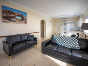 a living room with two leather couches and a kitchen at API Pelican Beach Front Apartments Kalbarri in Kalbarri