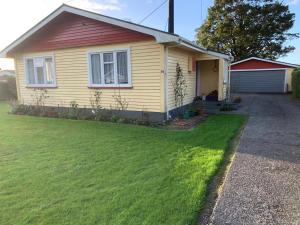 a small yellow house with a grass yard at Poppas House in Harihari