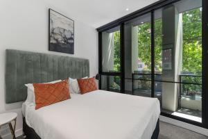 sypialnia z białym łóżkiem i dużymi oknami w obiekcie The Eminence Apartments by CLLIX w Melbourne