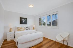 a white bedroom with a bed and two windows at Bermagui Townhouse - Amazing views & location in Bermagui