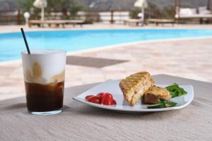 a plate of food and a drink on a table near a pool at Amorgion Village in Katapola