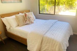 una camera da letto con un letto bianco con cuscini e una finestra di Skyview Cottage a Leura
