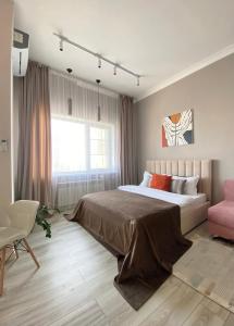 a bedroom with a large bed and a pink chair at Уютная студия с видом на Ботанический парк in Astana
