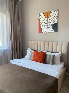 1 dormitorio con 1 cama grande con almohadas de color naranja y blanco en Уютная студия с видом на Ботанический парк en Astaná