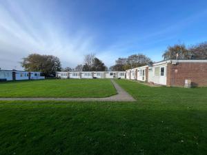 a large grassy field next to a brick building at 246, Belle Aire, Hemsby - Beautifully presented two bed chalet, sleeps 5, pet friendly, close to beach! in Great Yarmouth
