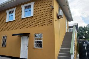 una casa amarilla con una puerta blanca y escaleras en Upstairs 2 Bedroom Avalon Regia Apartment, en Georgetown