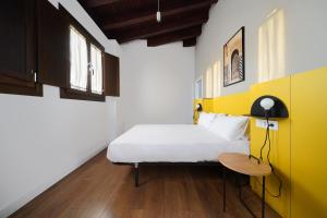 1 dormitorio con cama blanca y pared amarilla en numa I Vega Apartments, en Granada