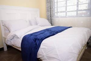 a white bed with a blue blanket on it at Crystal Homes Nanyuki Haven 2-BR Gem in Nanyuki