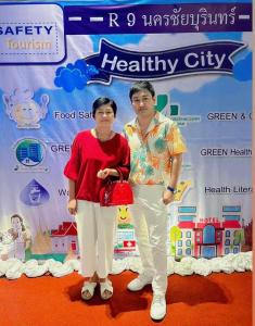 a man and woman standing in front of a health city sign at โรงแรมบ้านมะลิ ฮิลล์ เรสซิเด้นท์ in Kaeng Khlo