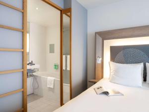 a bedroom with a bed and a bathroom with a tub at Novotel Mechelen Centrum in Mechelen