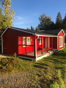 a red cabin with a deck in a field at Frykenbadens Camping in Kil