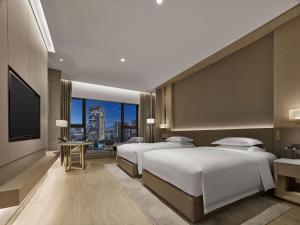 DoubleTree By Hilton Shenzhen Nanshan Hotel & Residences في شنجن: غرفة فندقية بثلاث اسرة وتلفزيون بشاشة مسطحة