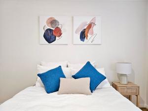 a white bed with blue pillows and three pictures on the wall at Cosy 3BR House, 7 mins drive to Macquarie Centre, 5 stars on AirB&B in Sydney