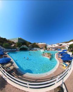 a large swimming pool with blue umbrellas and people in it at La chicca del porto in Santa Teresa Gallura