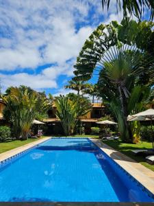 a blue swimming pool with palm trees and umbrellas at Casa Pipa Beleza in Pipa