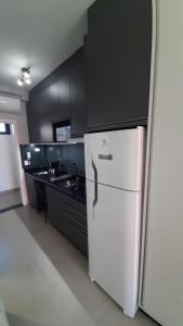 une cuisine avec un réfrigérateur blanc et des armoires noires dans l'établissement Studio 110 Maravilhoso Vista Mar Piscina Aquecida, à Matinhos