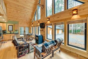 a log cabin living room with a fireplace and windows at Modern Cabin with Hot Tub and Sacandaga Lake Access! in Broadalbin