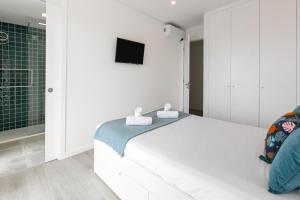 a white bedroom with a bed and a tv at Consolação Wave Beach House in Atouguia da Baleia