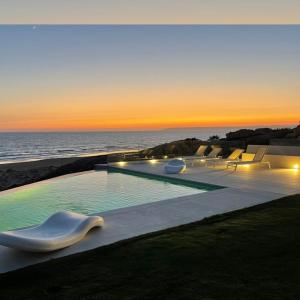a swimming pool with chairs and the ocean at sunset at Playa Blanca Zahara in Zahara de los Atunes