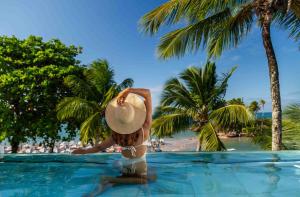 a woman in a hat standing in a swimming pool at a resort at Aqua by Sambass in Morro de São Paulo