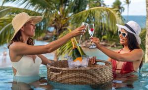two women in a swimming pool holding glasses of wine at Aqua by Sambass in Morro de São Paulo