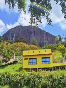 a yellow house on a hill with a mountain in the background at Descanso Bajo La Piedra Del Peñol in Guatapé