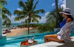 a woman sitting on a ledge next to a pool with a beach at Aqua by Sambass in Morro de São Paulo