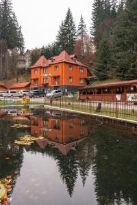 an orange building with a reflection in a body of water at Vila Bradul in Lacu Rosu