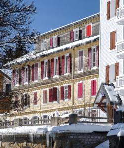 un grand bâtiment avec des fenêtres rouges à volets dans la neige dans l'établissement Location montagne le Revard, à Pugny-Chatenod