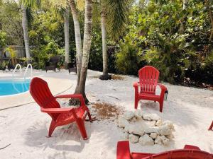 2 chaises rouges assises sur le sable près d'une piscine dans l'établissement Beach, Sand, Firepit and Pool, à Clearwater Beach