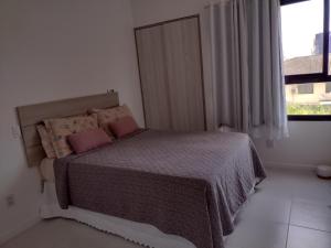 a bedroom with a bed with pink pillows and a window at Apt Estrada do coco- Lauro de Freitas in Lauro de Freitas