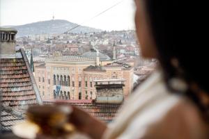 Una mujer mirando por una ventana a una ciudad en Hotel Herc Sarajevo en Sarajevo