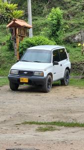 une voiture blanche garée sur un chemin de terre dans l'établissement Glamping Akaya, à Ibagué