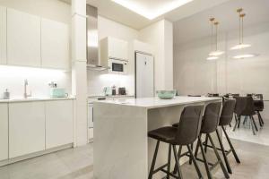 una cocina con armarios blancos y un bar con taburetes en Luxurious apartment in center with parking by REMS, en Málaga