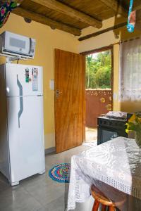 a kitchen with a refrigerator and a table and a door at Mini Chalés Madeira Beach in Ubatuba